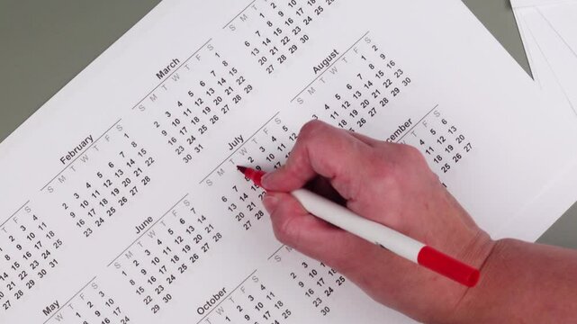Hand fills in a large wall calendar, counting down the days and marking 'Vacation' - the concept of planning and anticipating a vacation or holiday break.