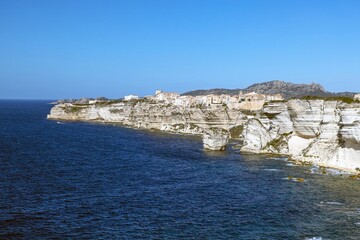 Historic Bonifacio on Corsica’s dramatic limestone cliffs against a clear blue Mediterranean sea and sky