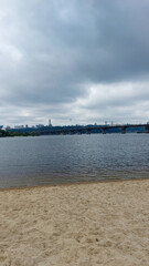 Sandy Beach with Bridge and Overcast Sky Over River