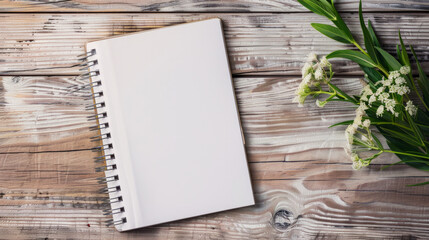 A blank spiral notebook on a rustic wooden surface next to a green plant and white flowers inviting creativity and inspiration