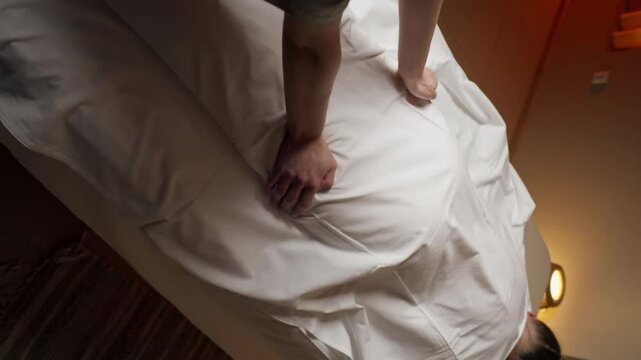 vertical video in massage parlor on a massage stand a girl is covered with a white cloth dry rubbing preliminary warming up of the hands of the masseur