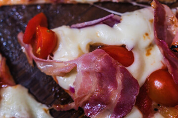 Delicious prosciutto pizza topped with fresh tomatoes and melted cheese served at a cozy pizzeria