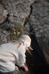 Child in Sun Hat Observing water on Rocky Coast