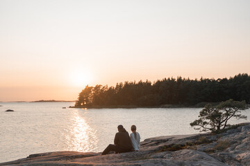Couple sitting on the rocky shore and watching ocean view and sunset