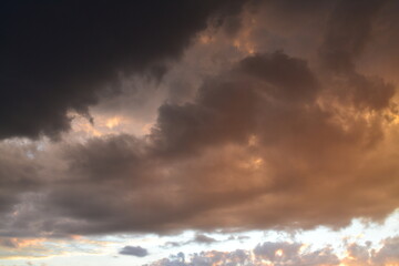 Bright unusual sunset city landscape orange pink rays above cityscape. Brutalist panel buildings appear as black silhouettes against a fiery orange-yellow sky dramatic lighting dark rain storm clouds