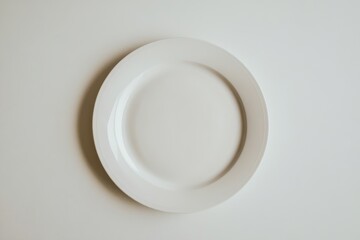 A white plate sits on a white table. The plate is empty and has no food on it. The table is clean and uncluttered. Concept of simplicity and minimalism. Empty space for logo or text, mockup