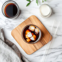A trendy flat lay of cold brew coffee with almond milk, a reusable glass straw, and a wooden coaster.