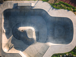 Aerial view of a modern skateboard park featuring diverse ramps and a skater performing tricks in the afternoon light