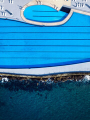 Aerial view of a blue swimming pool alongside the coastline during daylight hours