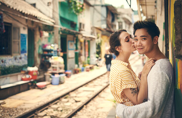 Fototapeta premium City, railway and couple with kiss for hug, travel adventure and explore vacation for anniversary. Interracial marriage, woman and man in portrait for admiration, love and bonding outdoor in Vietnam