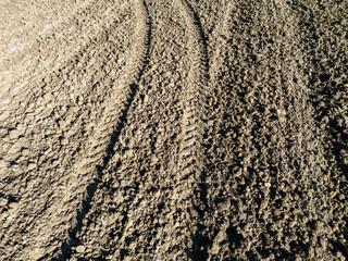 Close-up of fresh plowed soil showing tire tracks, highlighting the texture and pattern of agricultural land. Ideal for farming, agriculture, or environmental themes.