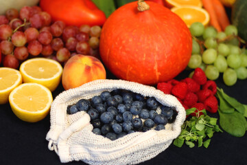 Round straw bag and various seasonal fruits and vegetables on dark background. Summer and fall produce. Selective focus.