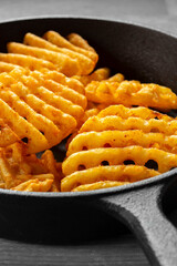 Waffle criss cross fries in a cast iron frying pan on a wooden cutting board. Unhealthy fast food concept