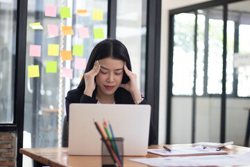 Fototapeta premium Asian female entrepreneur with headache sitting at company desk