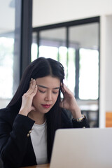 Fototapeta premium Asian female entrepreneur with headache sitting at company desk