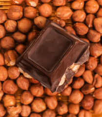 broken dark chocolate bar with hazelnuts on white backdrop, glowy golden background.top view of luxury desert, slabs one over another.empty space for text on box.