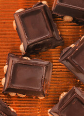 broken dark chocolate bar with hazelnuts on white backdrop, glowy golden background.top view of luxury desert, slabs one over another.empty space for text on box.