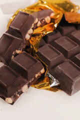 broken dark chocolate bar with hazelnuts on white backdrop, glowy golden background.top view of luxury desert, slabs one over another.empty space for text on box.