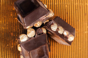 broken dark chocolate bar with hazelnuts on white backdrop, glowy golden background.top view of luxury desert, slabs one over another.empty space for text on box.