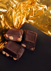broken dark chocolate bar with hazelnuts on white backdrop, glowy golden background.top view of luxury desert, slabs one over another.empty space for text on box.