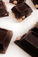 broken dark chocolate bar with hazelnuts on white backdrop, glowy golden background.top view of luxury desert, slabs one over another.empty space for text on box.