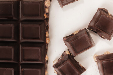 broken dark chocolate bar with hazelnuts on white backdrop, glowy golden background.top view of luxury desert, slabs one over another.empty space for text on box.