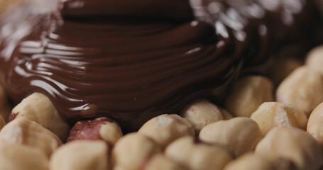 closeup covering roasted hazelnuts with melted dark chocolate