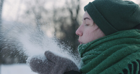 closeup of teen girl blowing snow from hands on cold winter day