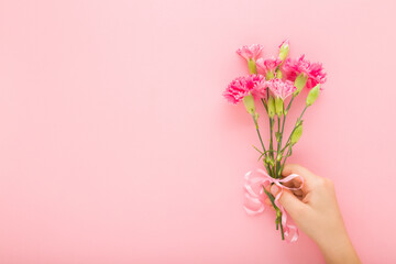 Little child girl hand holding fresh beautiful flower bouquet of pink carnations with ribbon on light pink wall background. Pastel color. Closeup. Empty place for text. Front view.