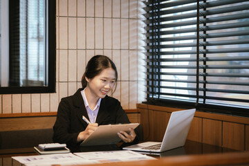 Young asian businesswoman analyzing financial chart using digital tablet and calculator in office
