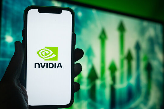 Hand Holding Phone with NVIDIA (NVDA) Logo and Monitor in the Background Showing Upward Green Arrows Suggesting Positive Stock Movement
