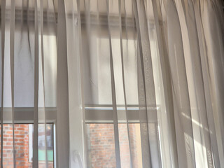 Bright sunlight filtering through sheer white curtains, creating a soft and airy atmosphere in a cozy room.
