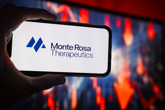 Hand Holding Phone with Monte Rosa Therapeutics (GLUE) Logo and Monitor in the Background Showing Red Arrows Pointing Down Suggesting Stock Decrease