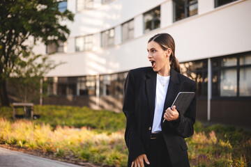 Amazed happy woman holding using digital tablet looking shocked about social media news, astonished business woman shopper consumer surprised excited by online win standing near office on the street.