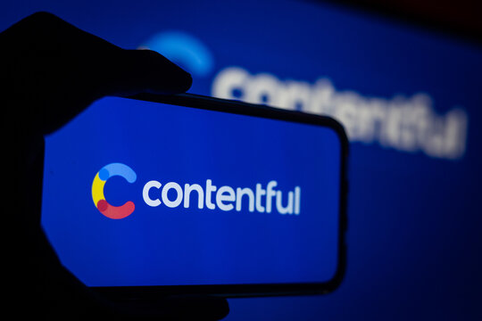 Silhouette of Hand Holding Phone with Contentful (CTF) Logo in Front of Computer Screen Displaying Contentful Content Management Solutions Logo
