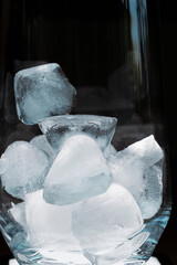 Vertical photo of a slightly dampened glass with ice on a dark background with copy space.