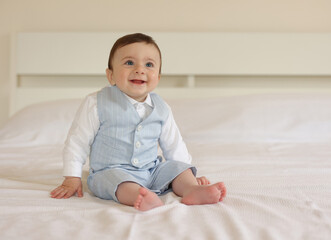 Fototapeta premium Baby boy sitting on bed wearing elegant suit smiling and looking up