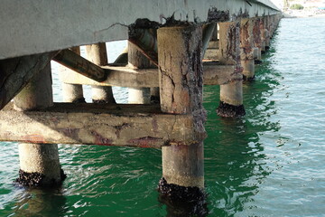 Concrete pier showing signs of deterioration and corrosion in green water