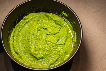Homemade italian pesto in a black bowl. Healthy herbs and ingredients for basic pesto. 
