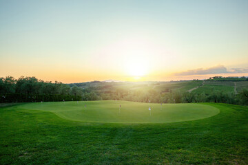 Putting green on golf course illuminated by setting sun over tuscany landscape