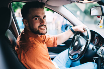 Man in casual clothing driving car and looking at camera