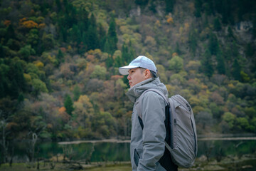 Hiker man wearing jacket and backpack standing by the mountain lake and looking at view, Dagu Glacier, Chengdu, China.	