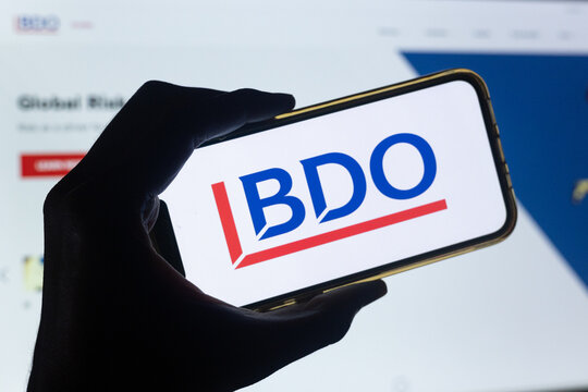 Silhouette of Hand Holding Phone with BDO Logo in Front of BDO Accounting and Consulting Services Website on Computer Screen
