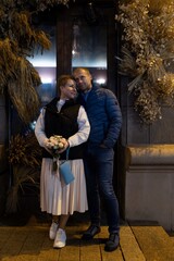 A couple walks through the city at night, holding hands and looking lovingly at each other