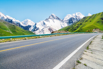 Asphalt highway road and green grass with snow mountain natural landscape under blue sky. road trip.