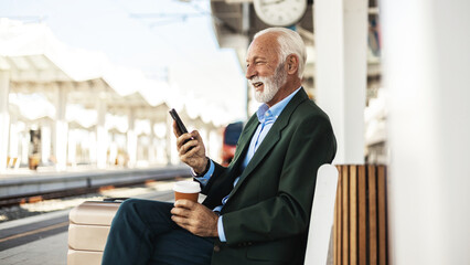 Modern business travel demands modern technology. Confident businessman talking on mobile phone while sitting outside the train station with a suitcase. Another success business trip.