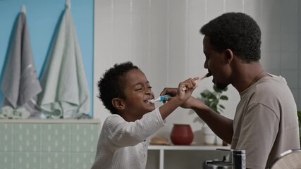 Medium shot of playful Black father and his little son having fun while brushing teeth of each other in stylish, bright bathroom in morning