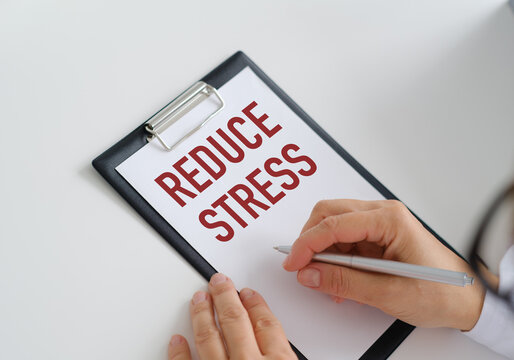 A person is writing the word Reduce Stress on a clipboard