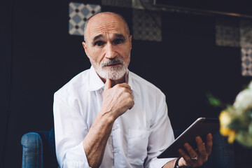Elderly man looking at camera while using tablet