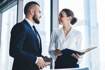 Executive with smartphone talking to smiling female secretary